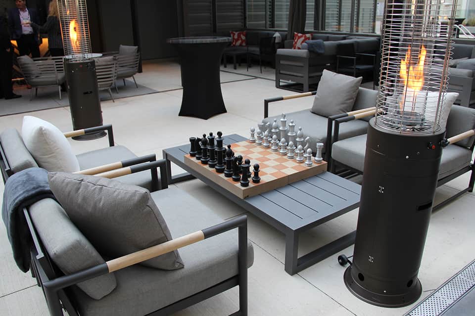 Elegant rooftop lounge with comfortable seating, chess set, heaters, and city views at dusk