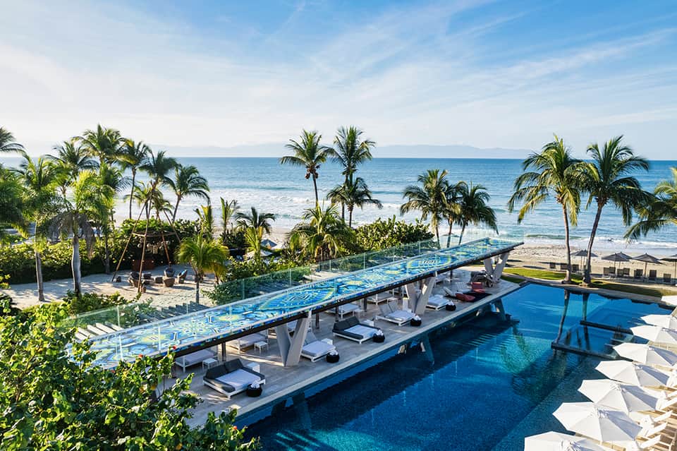 Oceanfront infinity pool with white loungers overlooking beach and palm trees