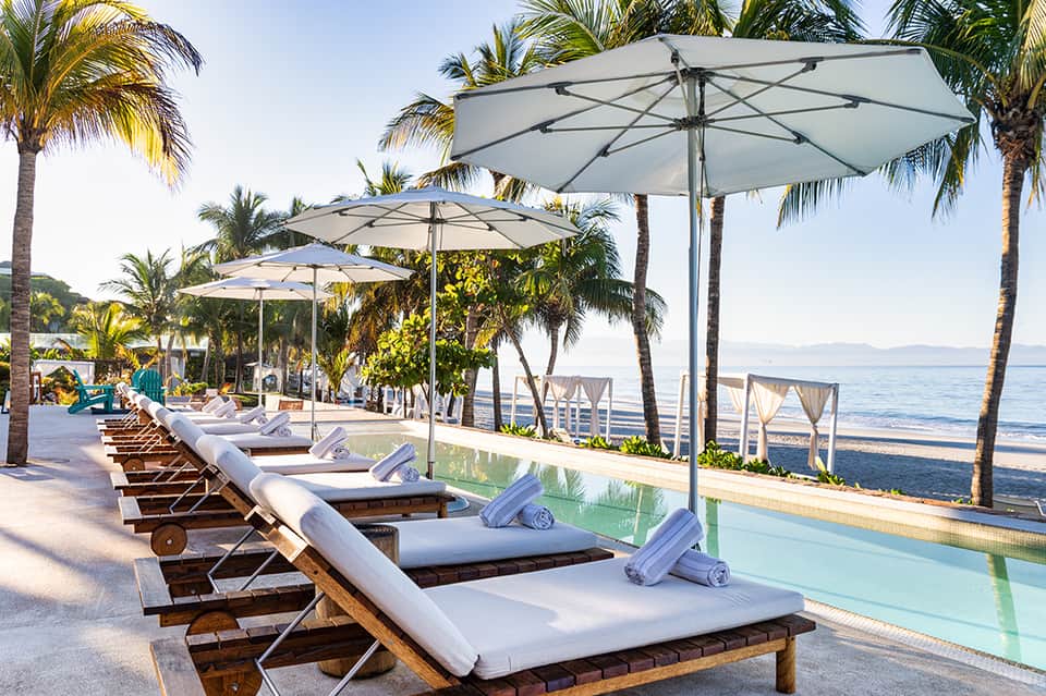 Beachfront sun loungers with umbrellas overlooking ocean and palm-lined shore