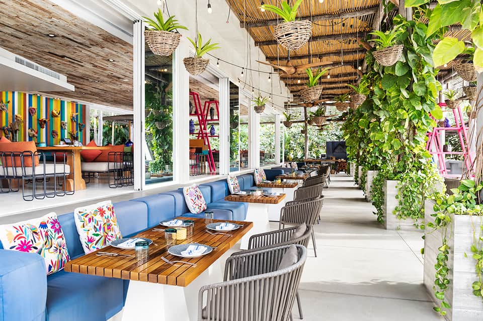 Modern resort restaurant with blue seating, wooden tables, hanging plants, and open-air design