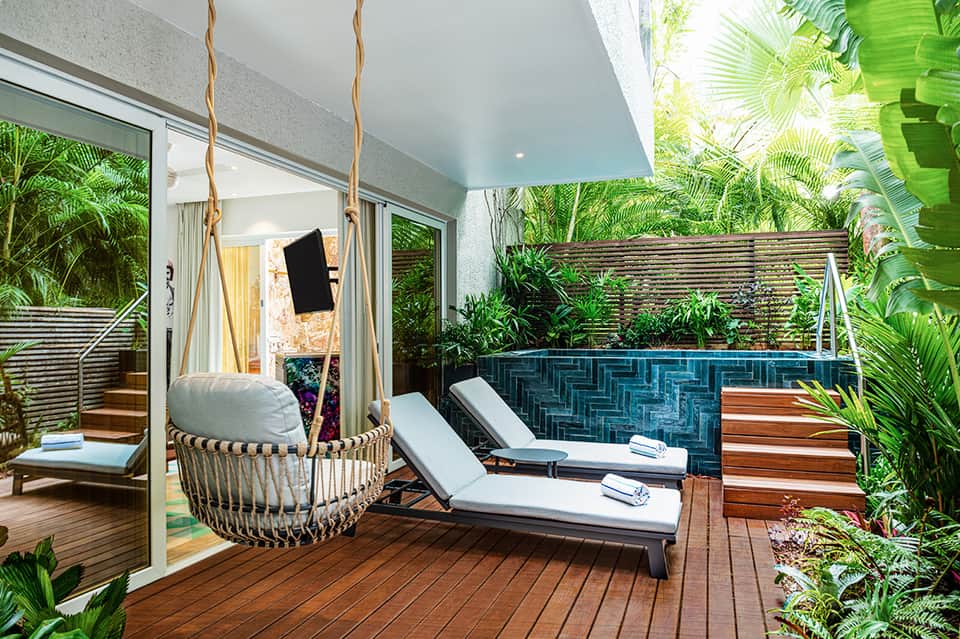 Modern villa terrace with hanging chair, hot tub, wooden deck, and tropical vegetation