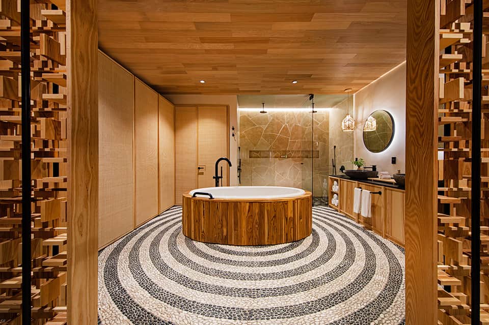 Luxury spa bathroom with wooden circular soaking tub, marble shower, and natural stone flooring