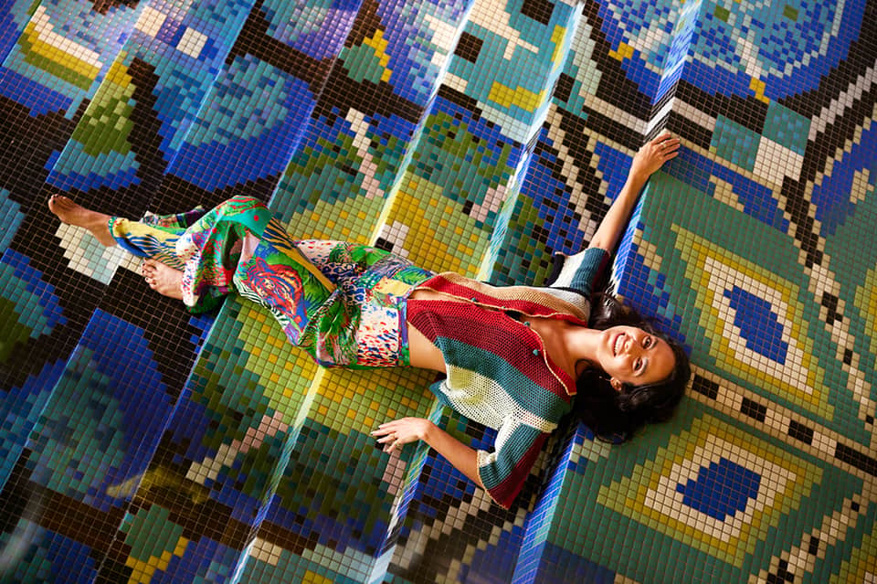 Woman lying on colorful mosaic pool floor in vibrant blue, green, and yellow tiles