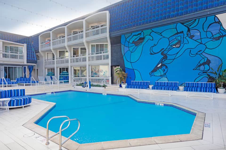Resort swimming pool with blue water, white lounge chairs with striped cushions, and art-decorated accent wall