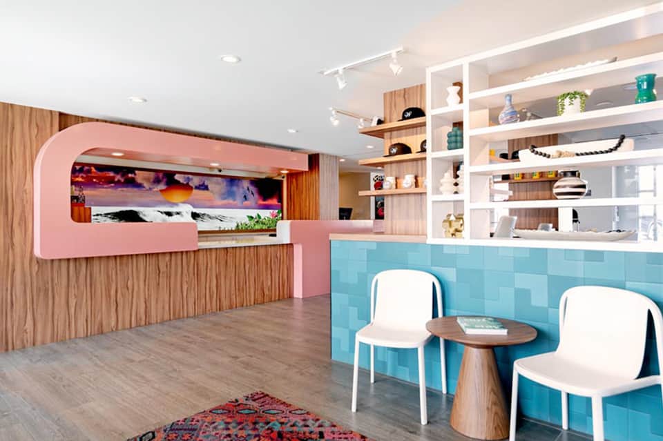 Modern hotel lobby with pink reception desk, turquoise tile accent wall, and white shelving