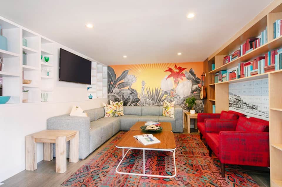 Colorful recreation room with gray sectional sofa, botanical wall mural, and vibrant red accent chair