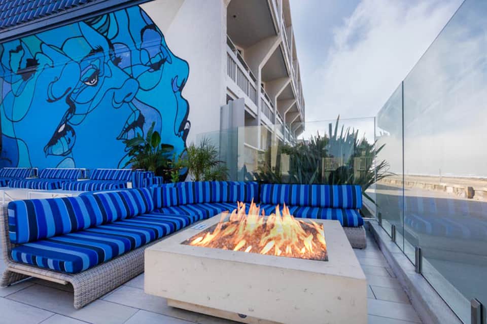 Rooftop terrace with blue striped seating, fire pit, and coastal city skyline view