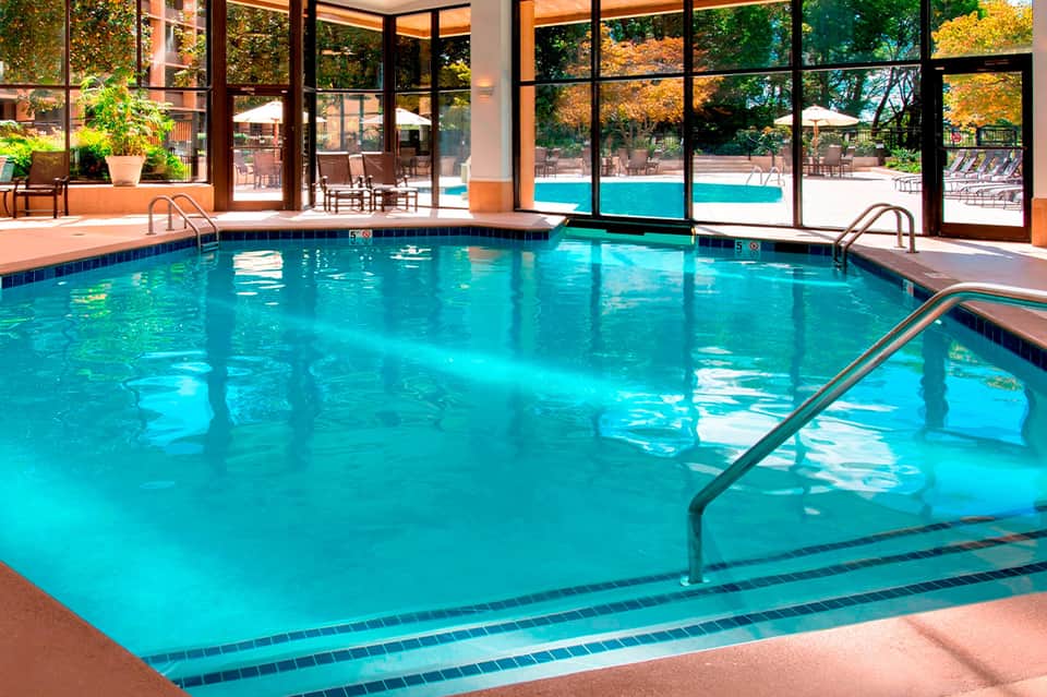 Indoor heated pool with turquoise water, large windows overlooking outdoor pool area