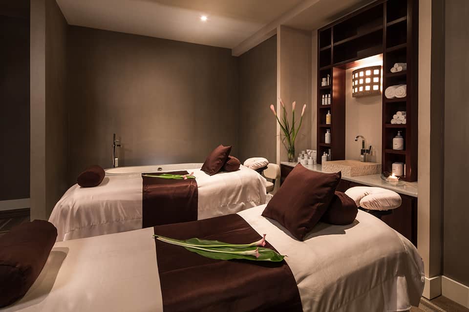 Modern spa treatment room with massage beds, brown accents, and ambient lighting