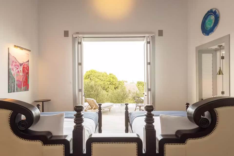 Luxury bedroom with twin beds, ocean view through open doors, and minimalist white décor