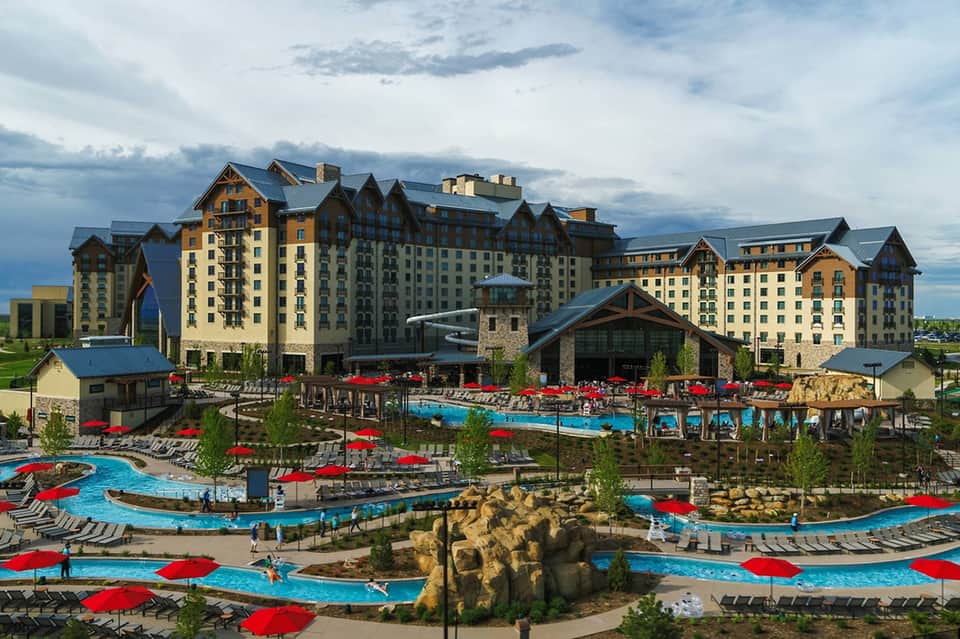 Large lodge-style resort with multiple pools, red umbrellas, water features, and mountain backdrop