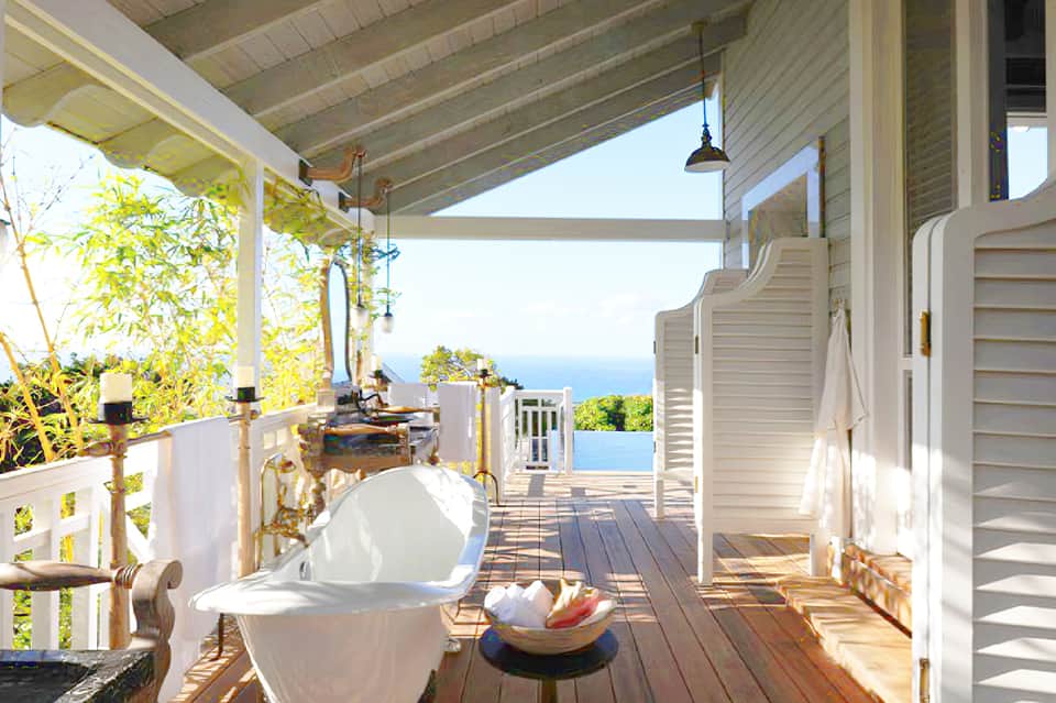Outdoor deck with freestanding bathtub, ocean view, and white railings at coastal villa