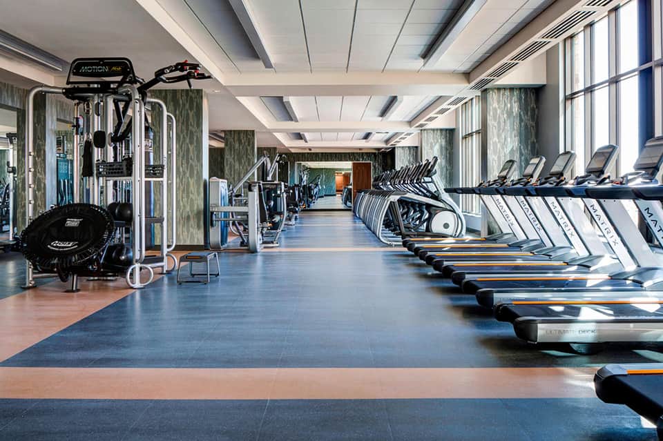 Modern hotel fitness center with rows of treadmills, exercise equipment, and floor-to-ceiling windows