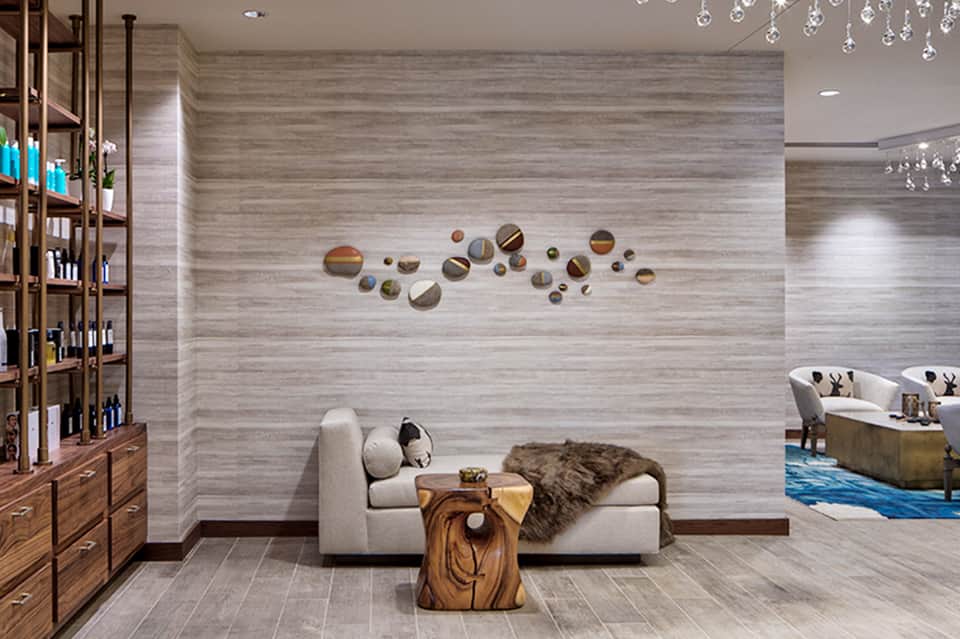 Spa lounge with beige seating, decorative circular mirrors, wood accents, and crystal chandelier