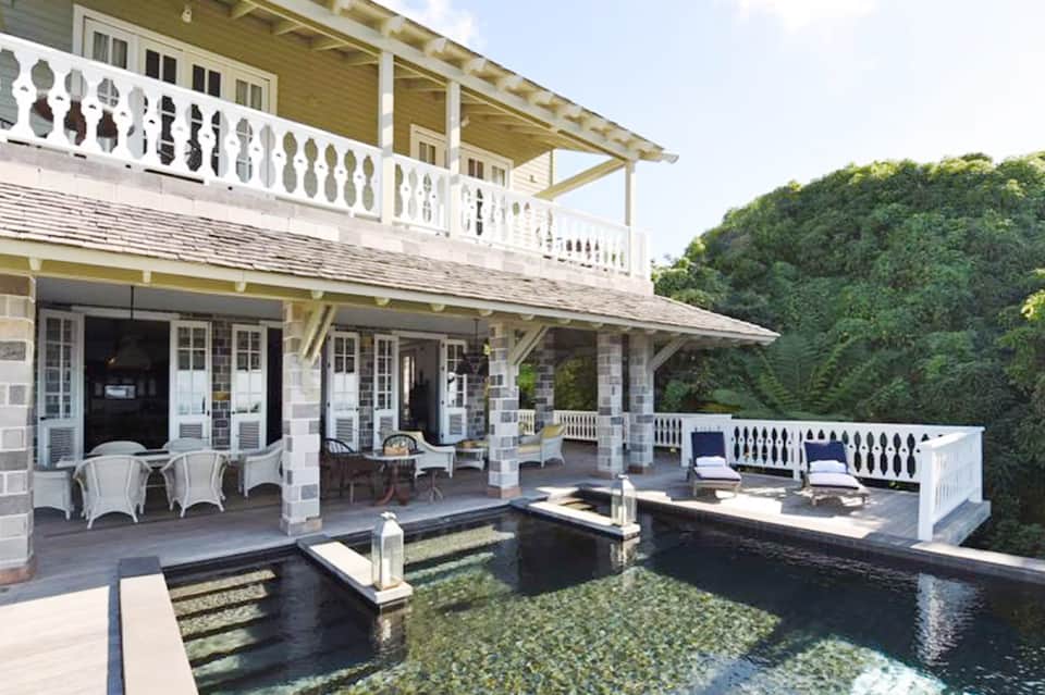 Upscale poolside villa with multi-level deck, white railings, reflecting pool, and woodland views