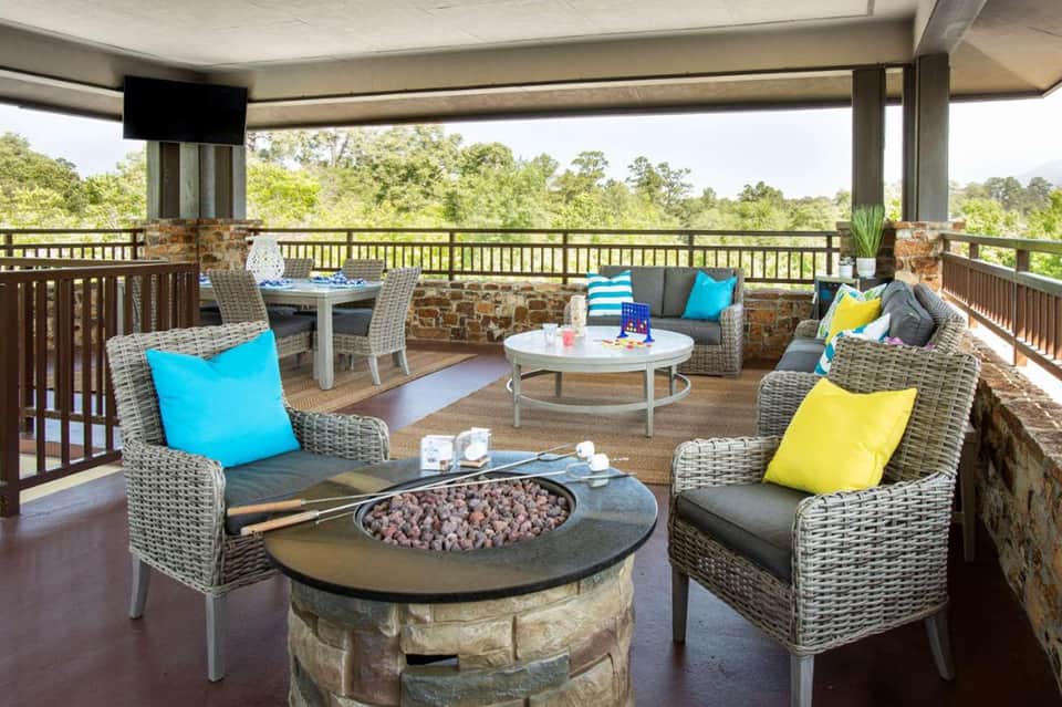 Elevated deck lounge with wicker furniture, fire pit, colorful pillows, and forest views