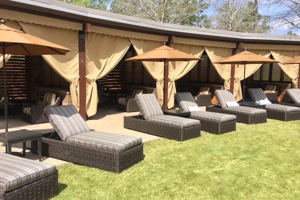 Outdoor spa cabanas with beige curtains and striped lounge chairs on green lawn