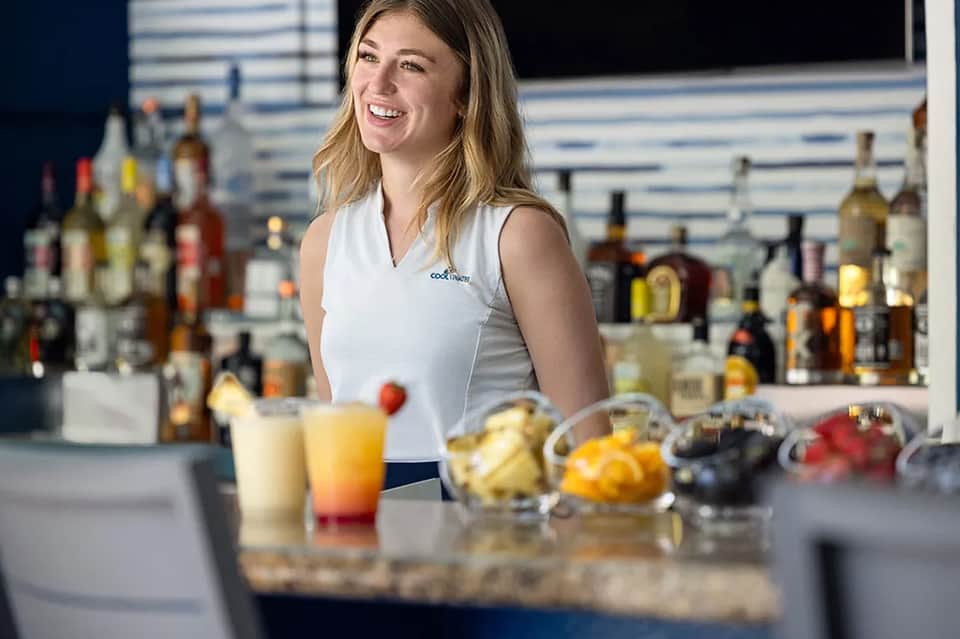 Female bartender at resort bar with cocktails and fresh fruit on counter