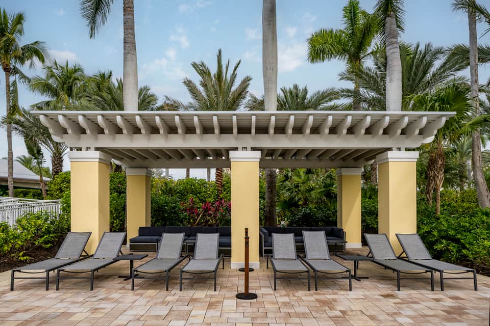 Lounge chairs under modern yellow pergola with palm trees and tropical landscaping