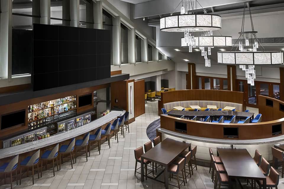 Modern hotel bar and lounge with curved counter, crystal chandeliers, and seating area
