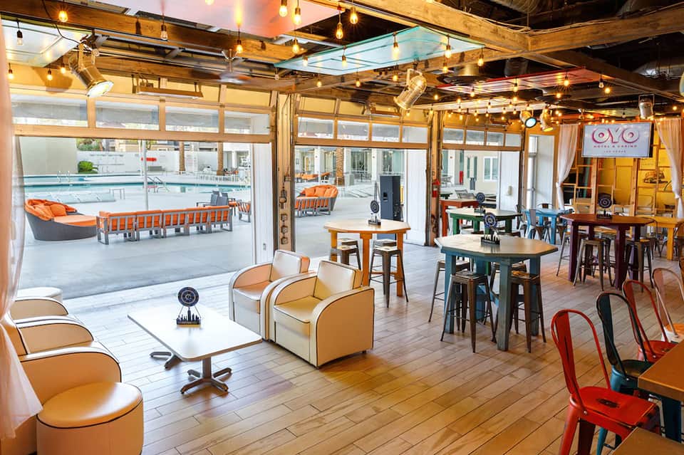 Casual resort pool bar and lounge with orange seating, glass doors, wooden ceiling, and pool views