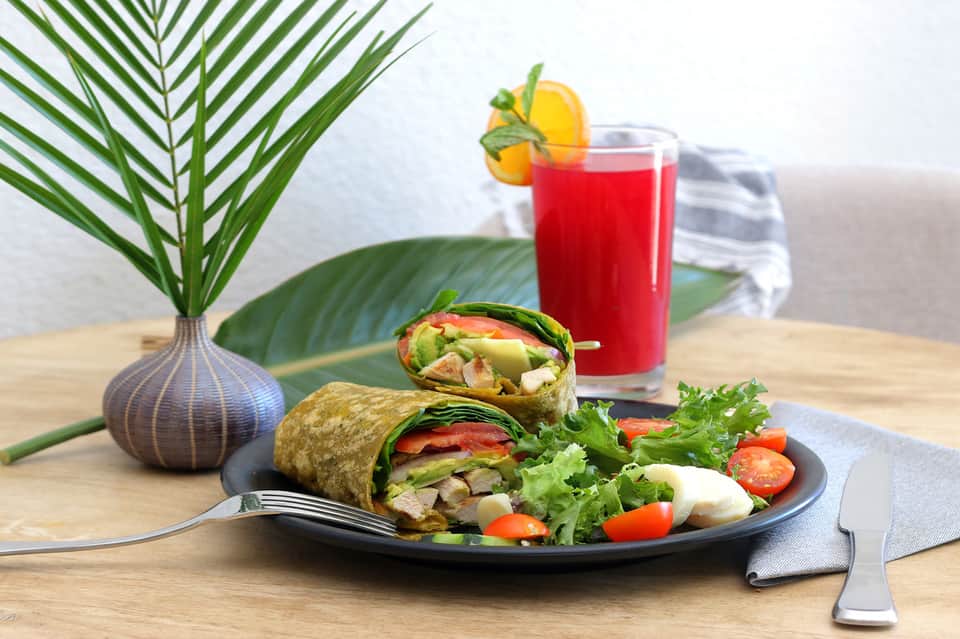 Healthy wrap lunch with fresh vegetables, juice, and tropical plant decor on wooden table