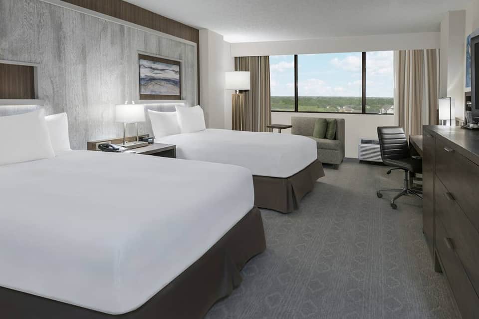 Modern hotel room with two queen beds, floor-to-ceiling windows overlooking landscape, and contemporary furnishings
