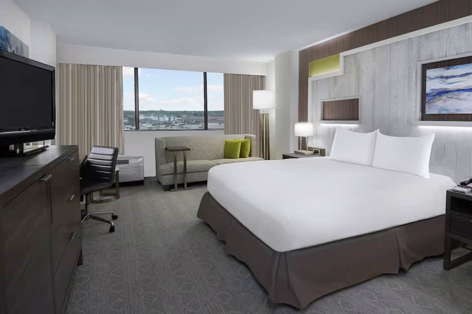 Modern hotel bedroom with bed, workspace, and panoramic city view