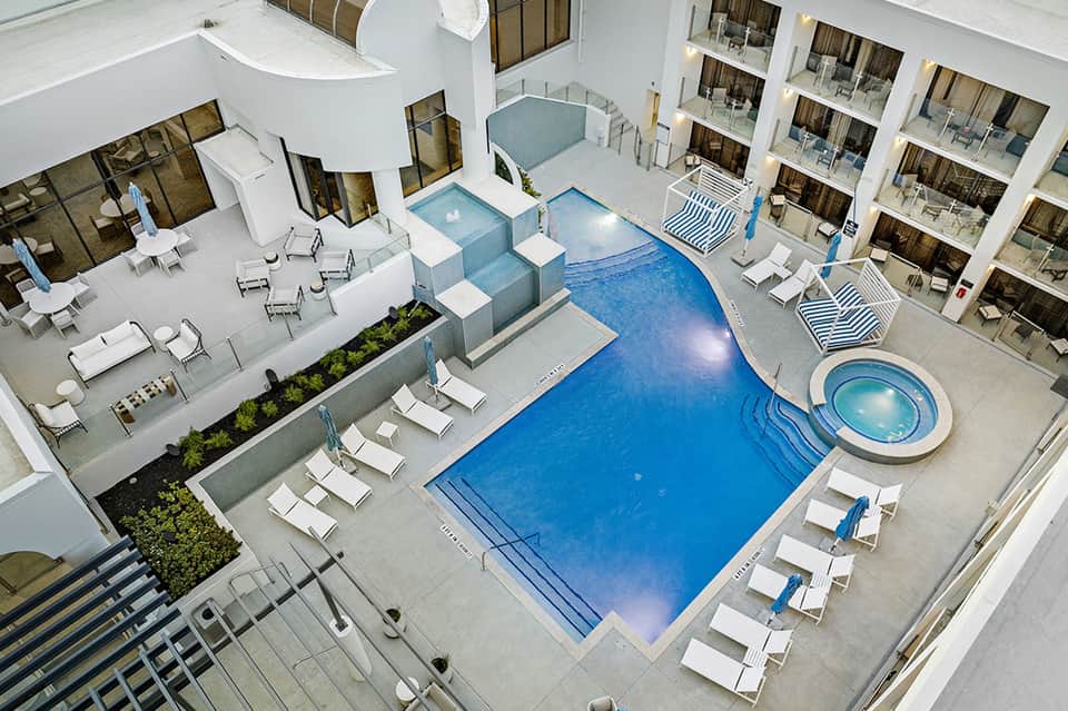 Aerial view of resort pool complex with loungers, spa, surrounding balconied rooms, and landscaping