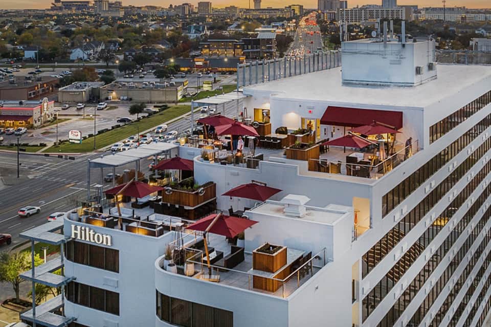 Hilton hotel rooftop with multiple lounge areas, burgundy umbrellas, and city skyline view