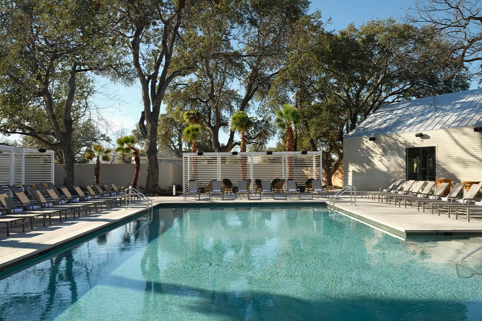 Rectangular resort pool with turquoise water, lounge chairs, and modern poolside buildings with trees