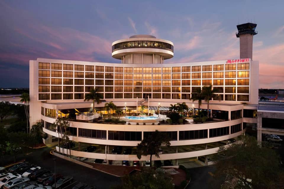Modern airport hotel with curved architecture, control tower, and illuminated pool deck at dusk