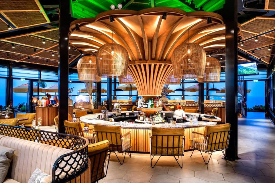 Upscale restaurant with shell-shaped lighting fixture, open kitchen counter, and panoramic window views