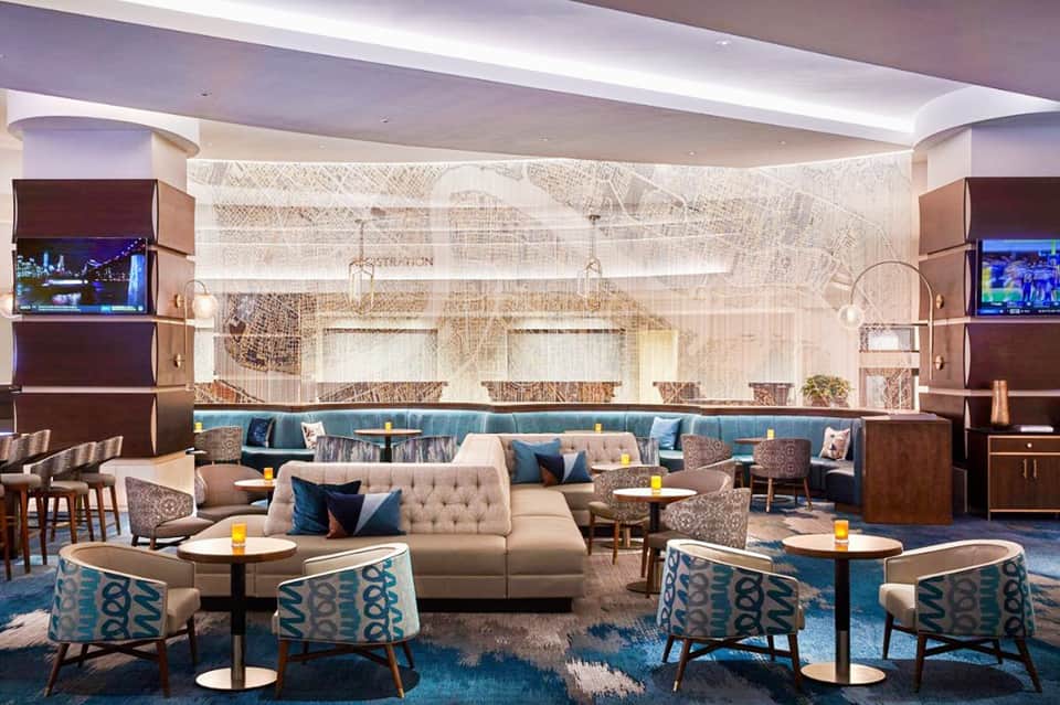 Sophisticated hotel lounge with curved beige sofa, blue accent chairs, warm lighting, and textured wall art