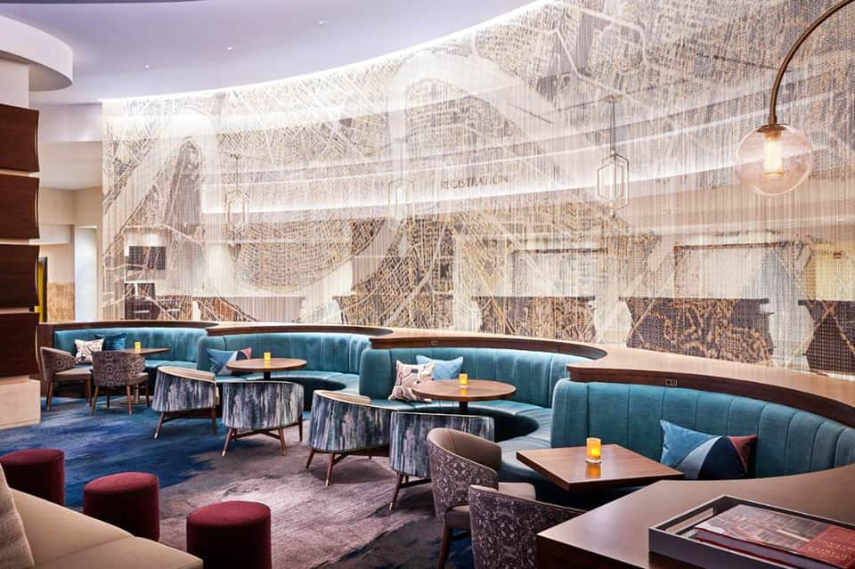 Modern hotel lounge with teal curved seating, decorative wall mural, and contemporary furnishings