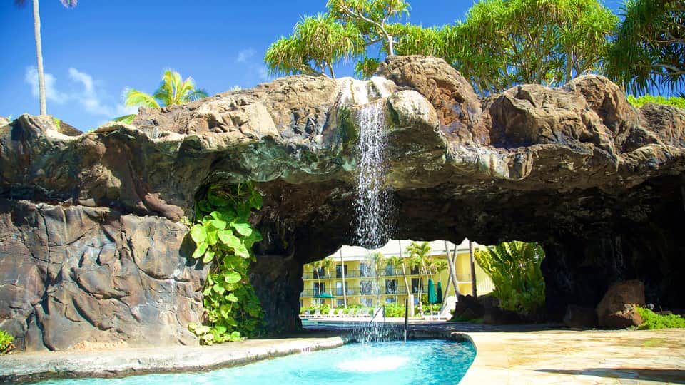 Tropical resort pool with waterfall beneath natural rock formations and palm tree canopy