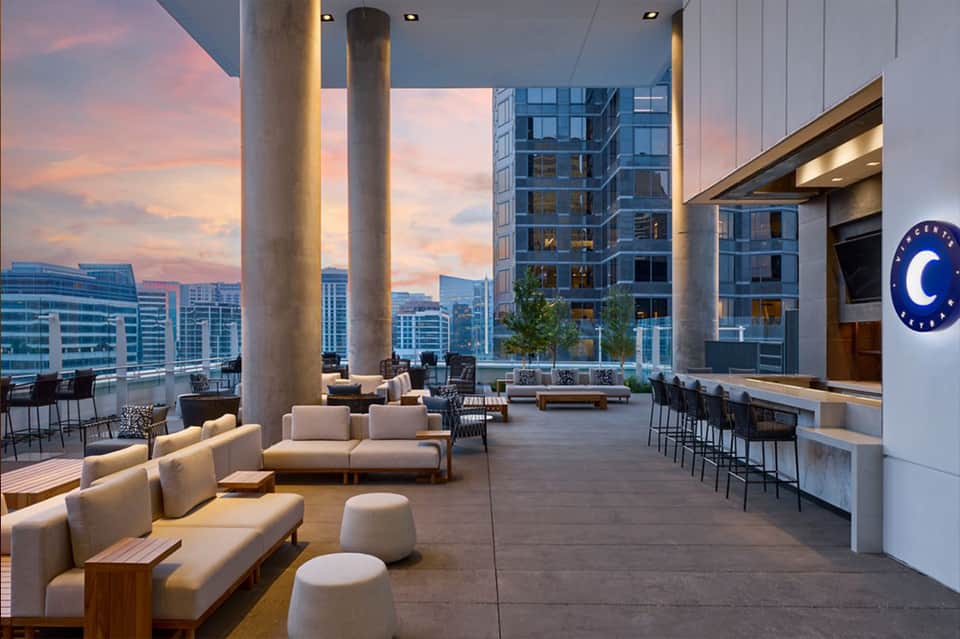 Modern hotel lounge with white seating, floor-to-ceiling windows, and sunset cityscape