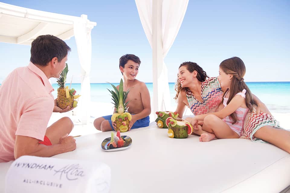 Family enjoying tropical drinks with pineapple garnishes on a beachfront cabana with ocean view