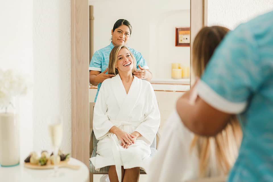 Spa service scene with massage therapist and client in white robe reflected in mirror