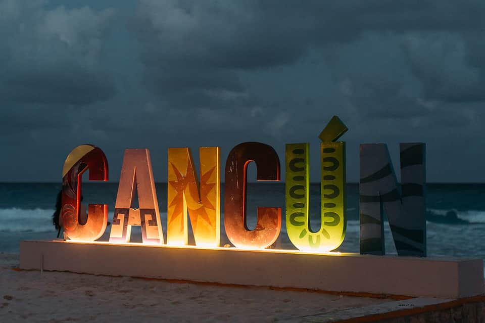 Illuminated Cancun sign on beach at dusk with stormy sky and ocean backdrop