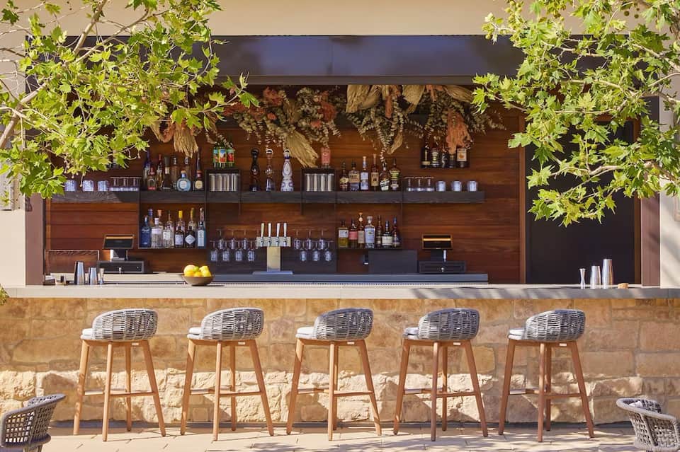 Outdoor tiki bar with wooden counter, wicker stools, and hanging plants