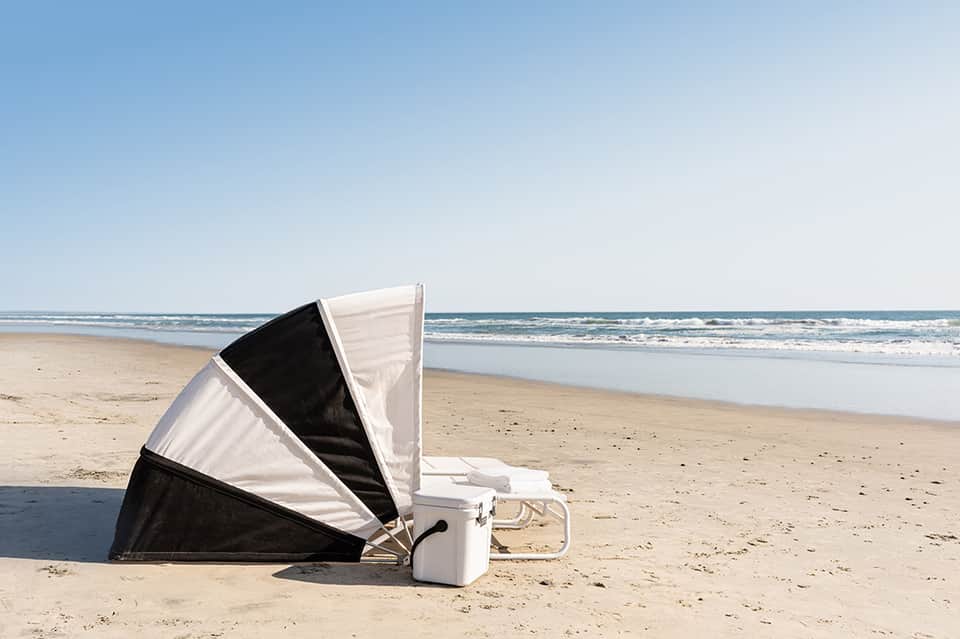 White and black beach tent set up on sandy shore with calm ocean and clear blue sky visible