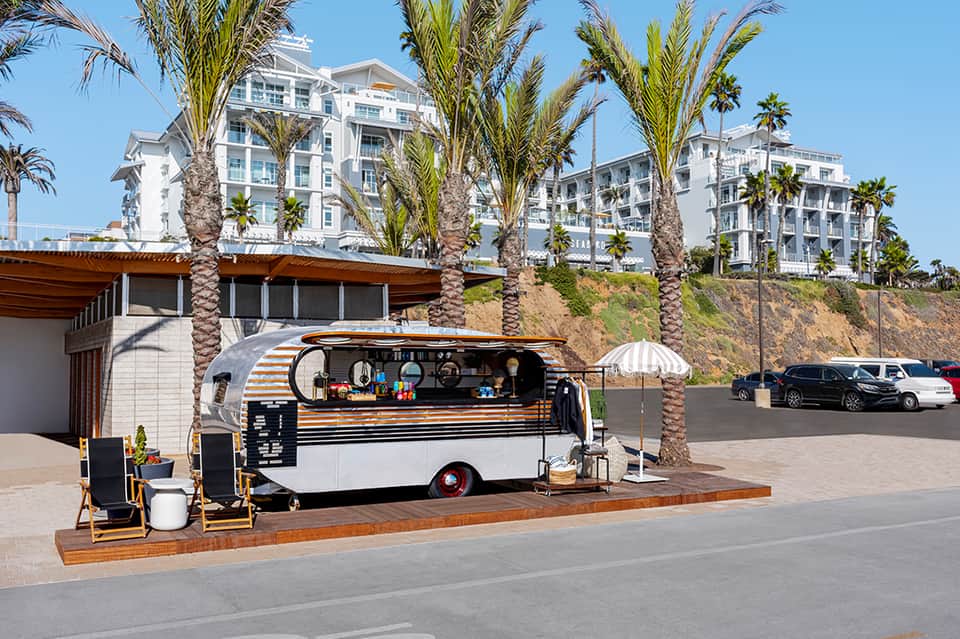 Food truck with orange striped awning parked in front of white beachfront apartment buildings