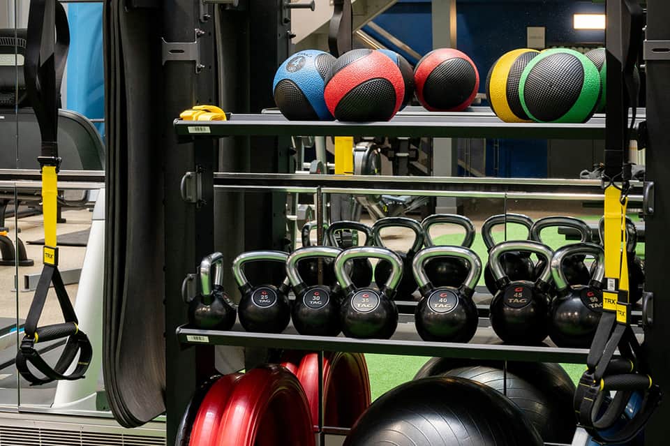 Fitness center shelf displaying colorful medicine balls and kettlebells for strength training