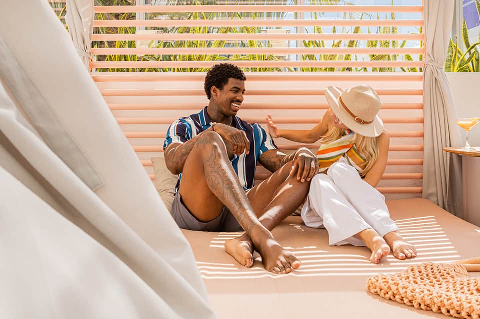 Couple relaxing on cabana daybed with sheer white curtains and tropical garden views