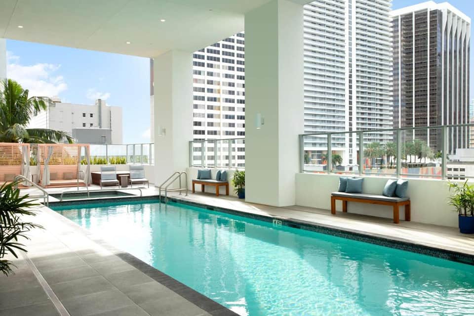 Modern indoor pool on upper floor with city and ocean views, floor-to-ceiling windows, and contemporary seating