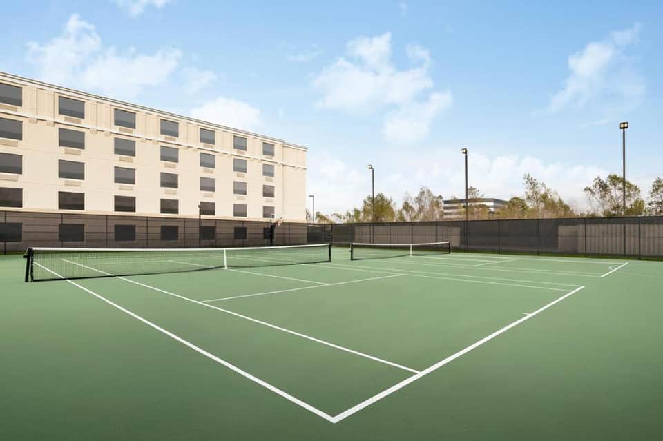 Outdoor tennis courts with green playing surface adjacent to modern hotel building