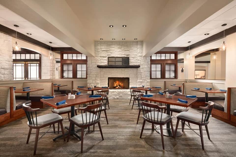 Modern resort dining room with fireplace, wooden furnishings, white stone walls, and contemporary lighting