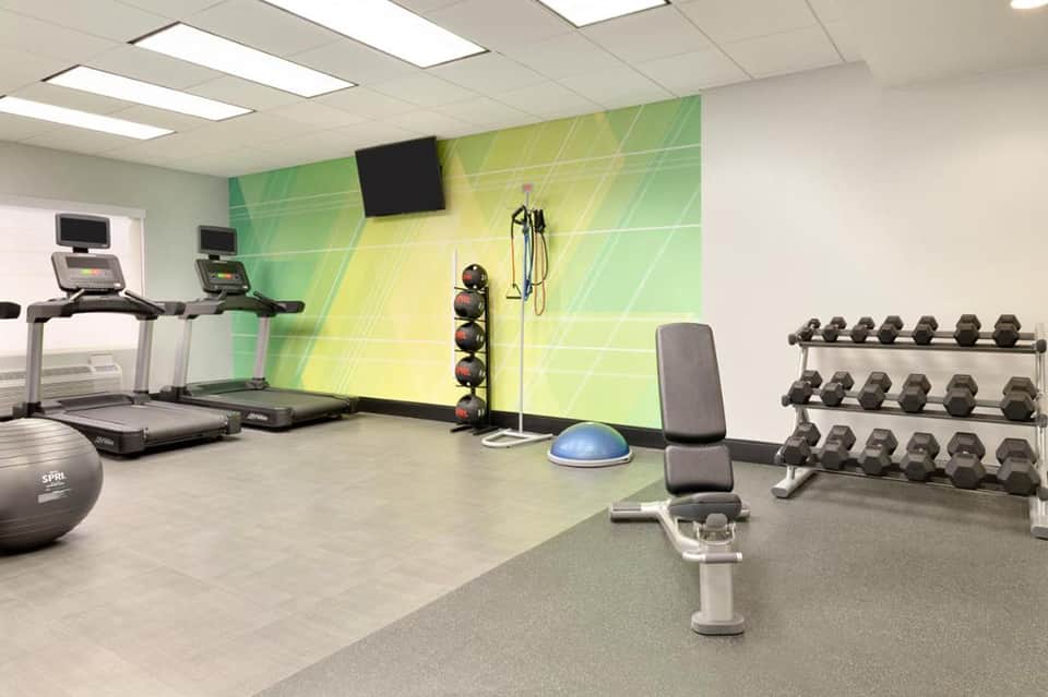 Fitness center with treadmills, dumbbells, exercise equipment, and green accent wall