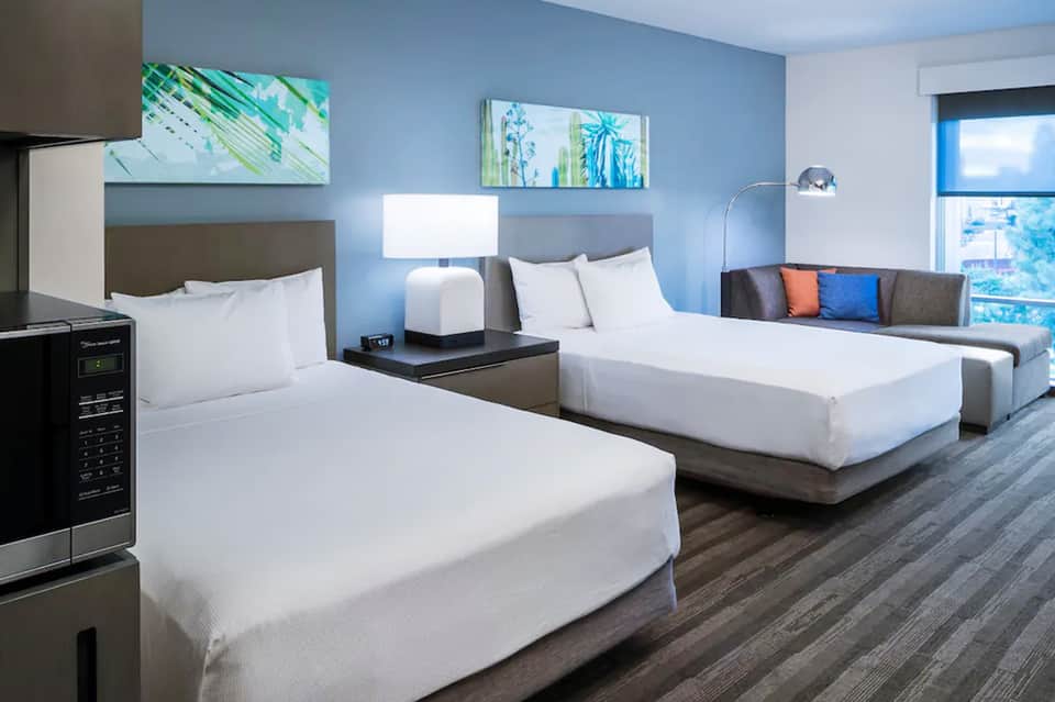 Modern hotel room with two queen beds, blue walls, ocean view, and contemporary furnishings